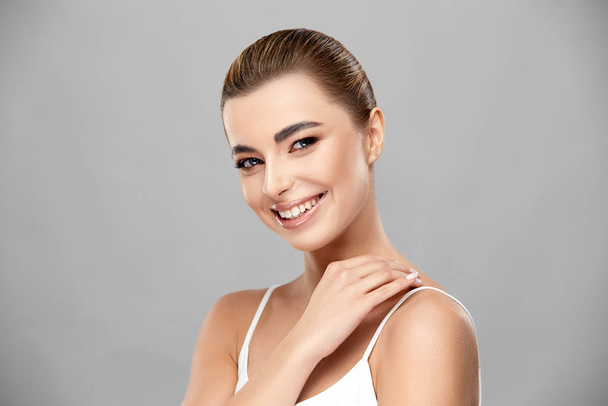 elegant lady with perfect skin and light make-up smiling to camera and touching her shoulder - Photo, Image