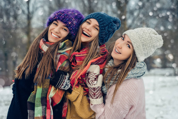 Trois amies à l'extérieur en bonnets tricotés s'amusent par temps froid enneigé. Groupe de jeunes amies à l'extérieur dans le parc d'hiver
. - Photo, image