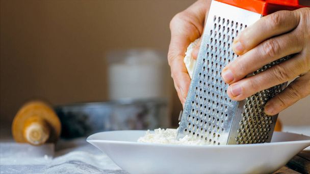 Close-up hands of mature woman is rubs a cheese on a steel grater - Фото, изображение