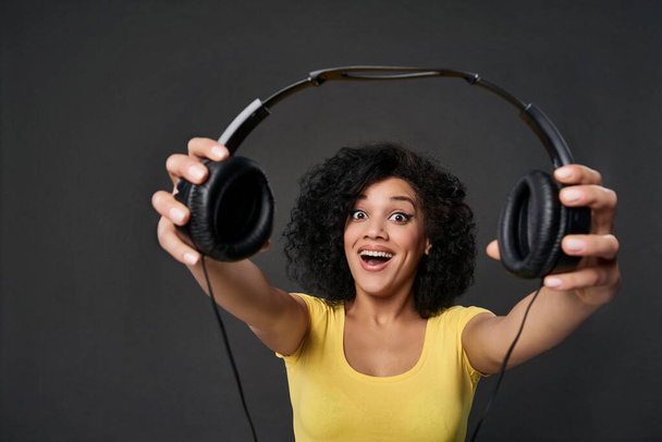 Excited woman giving you headphones, studio shot - Foto, imagen