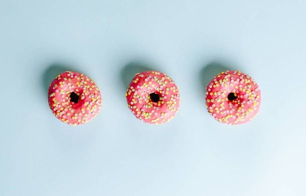 High angle closeup shot of three donuts with red cream on a light blue surface - Fotoğraf, Görsel