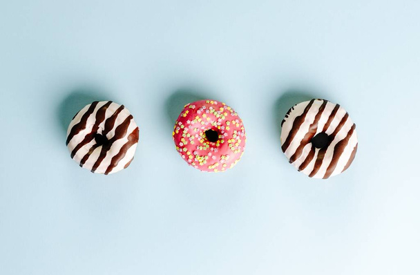 High angle closeup shot of three donuts on a light blue surface - perfect for a cool wallpaper - Fotoğraf, Görsel