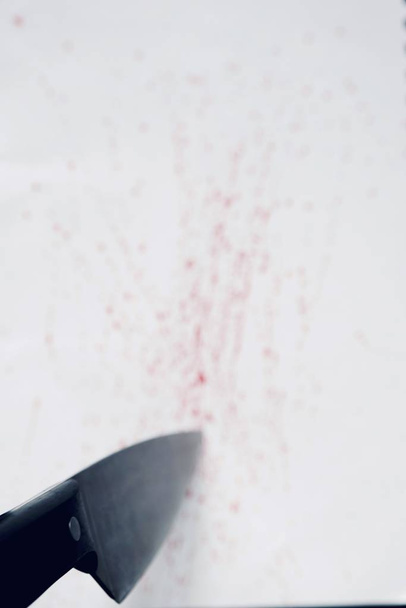 A vertical high angle shot of a knife pointing at a white surface with drops of blood on it - Foto, Bild