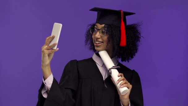 χαμογελαστός Αφροαμερικάνος απόφοιτος που παίρνει selfie απομονωμένη σε μωβ  - Πλάνα, βίντεο