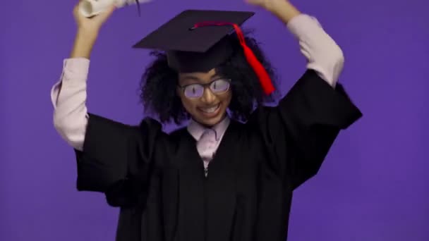 smiling african american graduate dancing with diploma isolated on purple  - Footage, Video