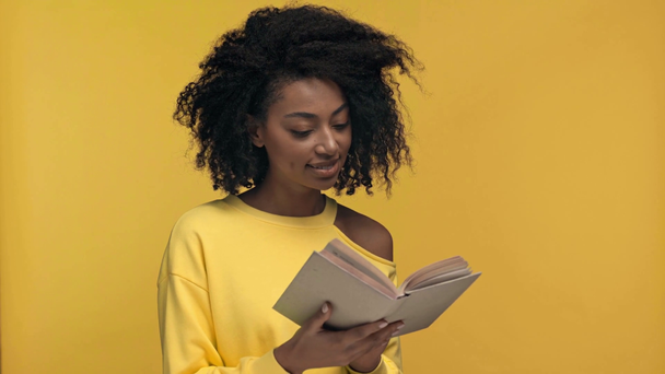 усміхнена афроамериканська жінка читає книгу ізольовано на жовтому
 - Кадри, відео