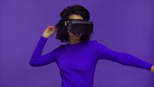 smiling african american woman in vr headset shooting isolated on purple  - Footage, Video