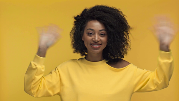 lächelnde Afroamerikanerin klopft und winkt isoliert auf gelb - Filmmaterial, Video