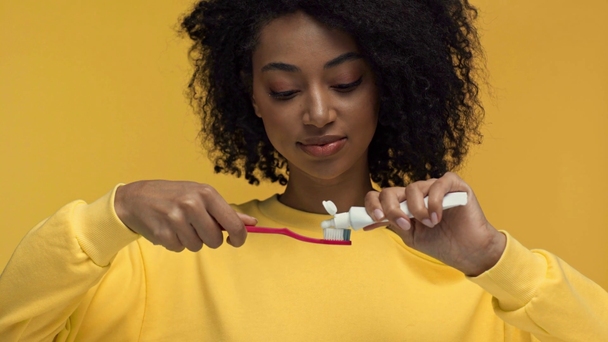 glimlachen Afrikaans amerikaanse vrouw knijpen tandpasta geïsoleerd op geel - Video