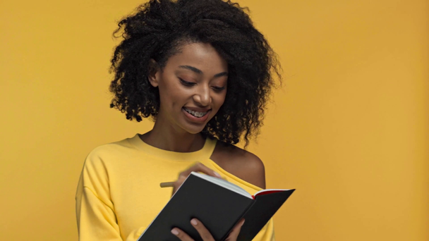 mujer afroamericana pensativa escribiendo en cuaderno aislado en amarillo
 - Imágenes, Vídeo