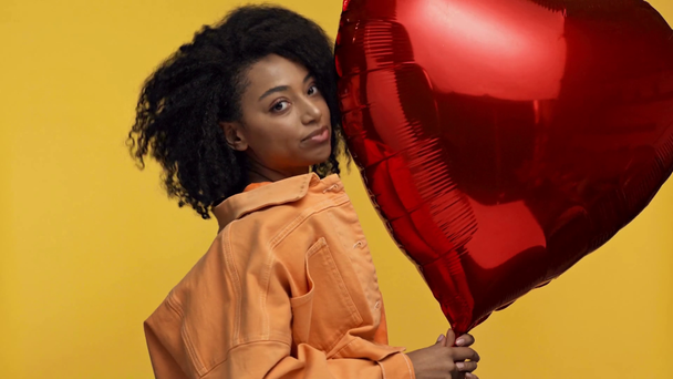 smiling african american woman holding balloon isolated on yellow - Footage, Video