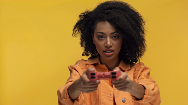 KYIV, UKRAINE - NOVEMBER 7, 2019: smiling african american woman playing with gamepad isolated on yellow - Séquence, vidéo