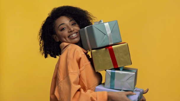 sonriente mujer afroamericana sosteniendo regalos aislados en amarillo
 - Imágenes, Vídeo
