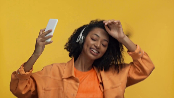 Gülümseyen Afrikalı Amerikalı kadın sarıda izole edilmiş müzik dinliyor. - Video, Çekim