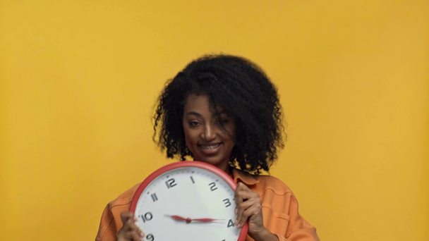 smiling african american woman dancing with clock isolated on yellow - Footage, Video