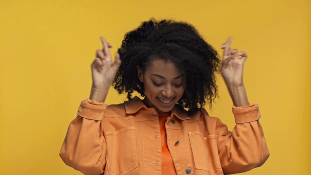 χαμογελαστή Αφροαμερικανή γυναίκα που δείχνει σταυρωμένα δάχτυλα απομονωμένη στο κίτρινο - Πλάνα, βίντεο