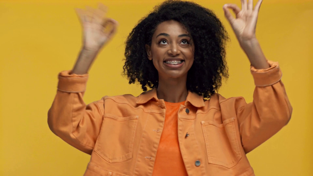 usmívající se africká americká žena ukazuje ok izolované na žluté - Záběry, video