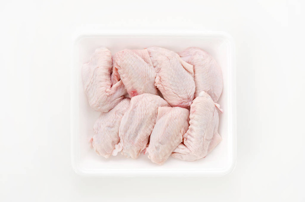 Asas de frango cruas e não cozidas em um recipiente de plástico branco
 - Foto, Imagem