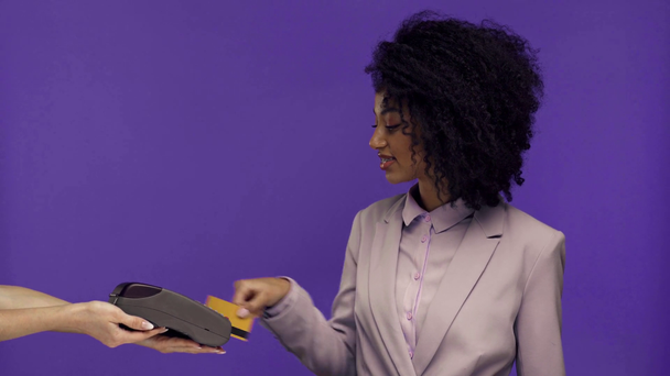 紫色で区切られたクレジットカードで支払う女性の保有端末とアフリカ系アメリカ人のビジネス女性のクロップドビュー  - 映像、動画