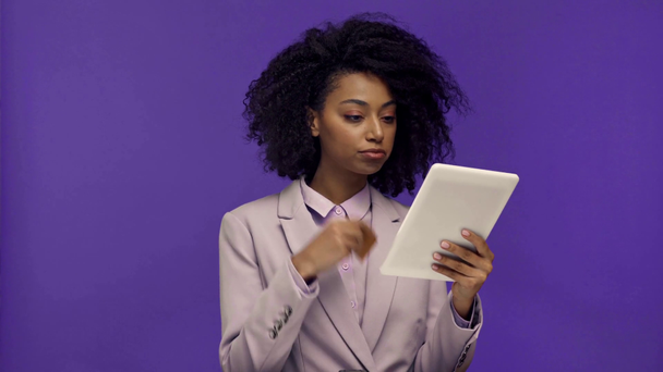 pensativa mujer de negocios afroamericana utilizando tableta digital aislada en púrpura
  - Metraje, vídeo