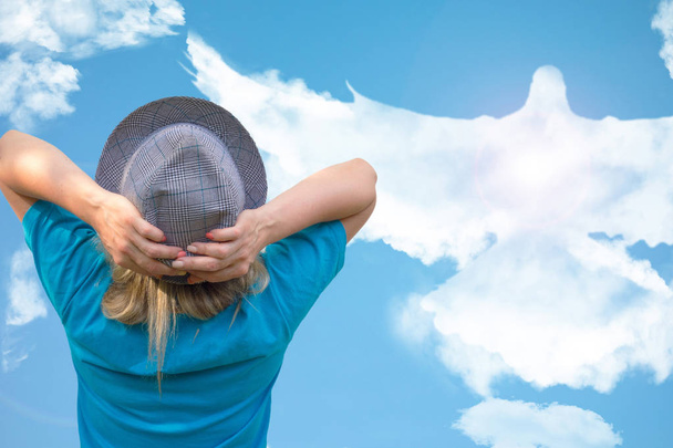 Κορίτσι με καπέλο κοιτάζει μεγάλο πουλί περιστέρι σε σχήμα σύννεφο που πετάει στο  - Φωτογραφία, εικόνα
