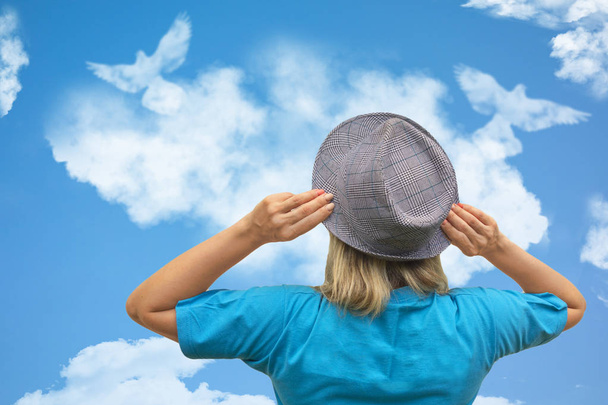 Mädchen mit Hut sieht Taubenvögel in Wolkenform schweben in blauem Himmel - Foto, Bild