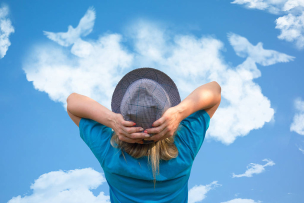 Chica en sombrero mira a los pájaros paloma en forma de nube se eleva en el cielo azul
 - Foto, Imagen