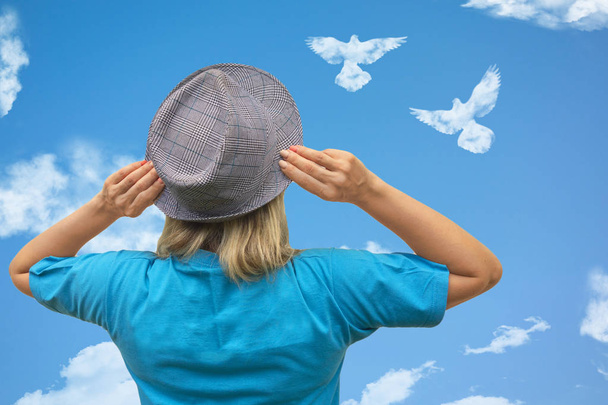 Chica en sombrero mira a los pájaros paloma en forma de nube se eleva en el cielo azul
 - Foto, Imagen