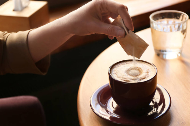 Woman adding sugar to aromatic coffee at table in cafe, closeup - Φωτογραφία, εικόνα