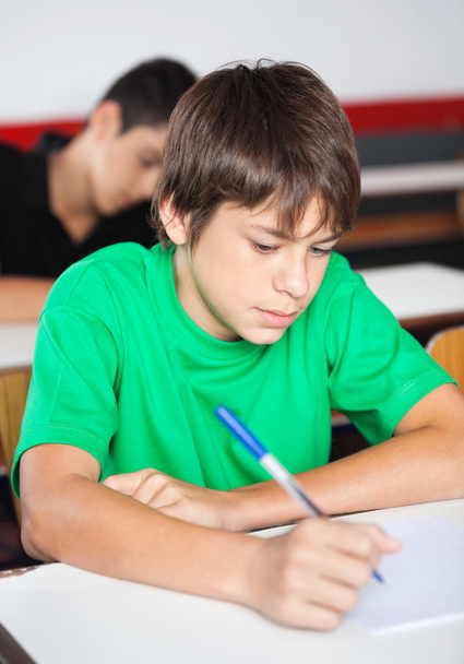 Teini-ikäinen koulupoika kirjoittaa työpöydällä tutkimuksen aikana
 - Valokuva, kuva