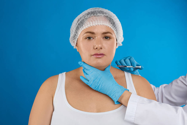 Woman with double chin getting injection on blue background. Cos - Фото, изображение