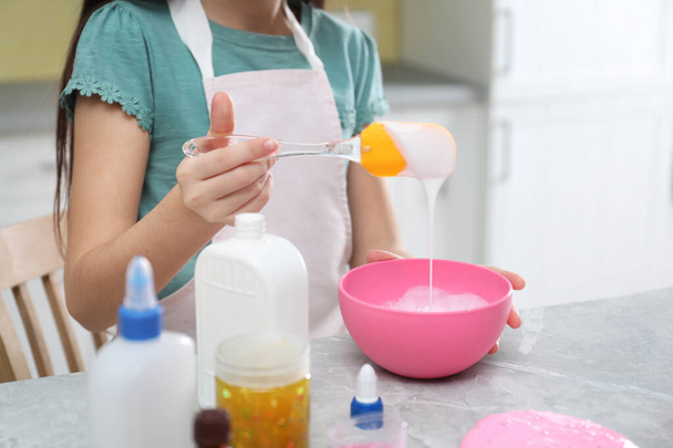 Little girl mixing ingredients with silicone spatula at table in kitchen, closeup. DIY slime toy - Fotoğraf, Görsel