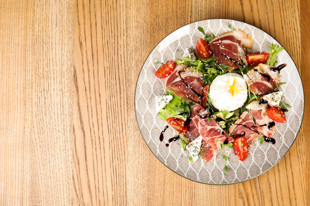 Delicious prosciutto salad with vegetables served on wooden table, top view. Space for text - Φωτογραφία, εικόνα