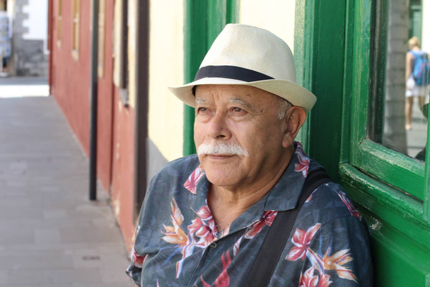 Tender senior homme portant un chapeau assis à l'extérieur pendant la journée
  - Photo, image