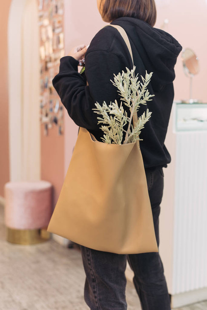 Dziewczyna w czarnym garniturze i torba z klientem na ramieniu. Zielona roślina w beżowym shopperze. Modna dziewczyna w centrum handlowym - Zdjęcie, obraz