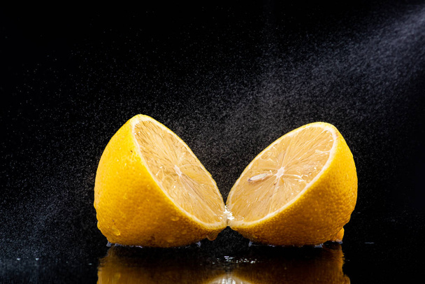 halves of a whole lemon with drops and splashes of water on a black background - Fotoğraf, Görsel