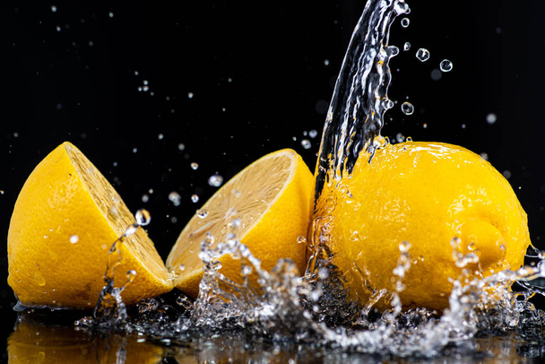 половинки целого лимона с капельками и брызгами воды на черном фоне
 - Фото, изображение