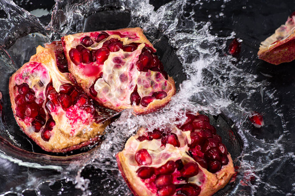 pieces of red pomegranate fruit with stream and splash of water on a black background - 写真・画像