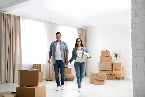 Happy couple in room with cardboard boxes on moving day - Foto, afbeelding