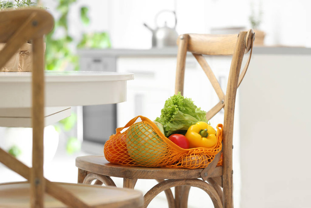 Net bag with vegetables on wooden chair in kitchen - Фото, зображення