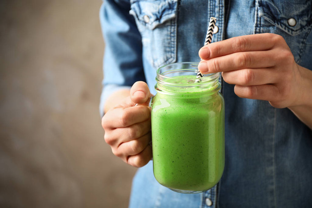Woman holding tasty kale smoothie on brown background, closeup - 写真・画像