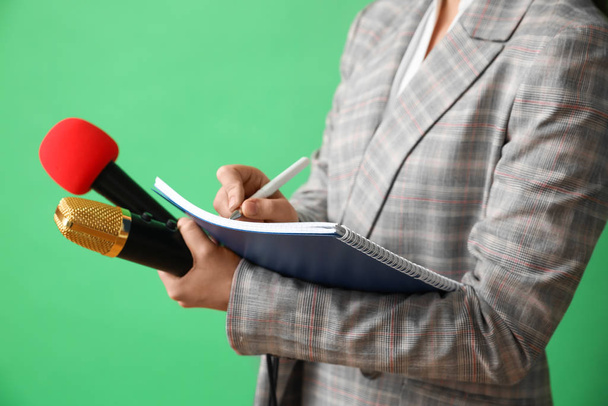 Journalist mit Mikrofon und Notizbuch auf grünem Hintergrund, Nahaufnahme - Foto, Bild