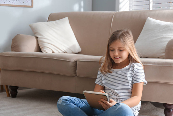 Cute little girl with notebook near couch at home. Space for text - Foto, immagini
