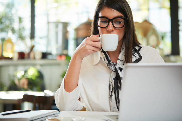 Attractive caucasian elegant brunette sitting in cafe, drinking coffee. On table is laptop. - Fotografie, Obrázek