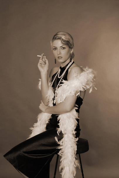 a woman dressed in the style of the 20's sitting on a bar stool with a cigarette. - 写真・画像