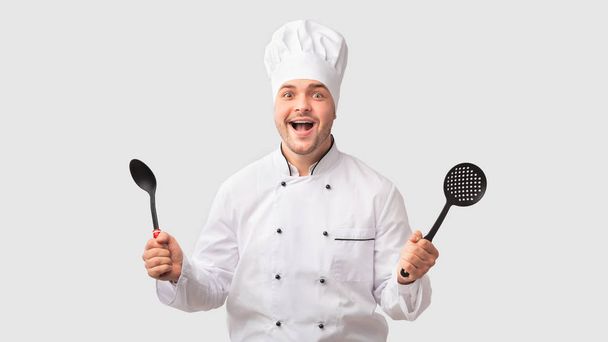 Возбужденный шеф-повар держит ковш и слотскую ложку, белый фон
 - Фото, изображение
