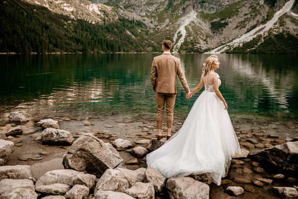 Νεαρή νύφη και γαμπρός ποζάρουν στη λίμνη Morskie Oko στα βουνά Tatra, στη νότια Πολωνία - Φωτογραφία, εικόνα