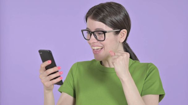 紫色の背景に携帯電話を使用して驚きの若い女性 - 写真・画像