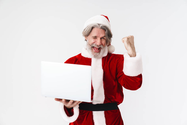 Retrato del hombre gris encantado haciendo gesto ganador y usando el ordenador portátil
 - Foto, imagen