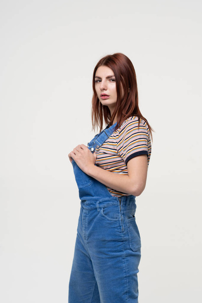 young beautiful girl is standing in blue overalls - Фото, изображение
